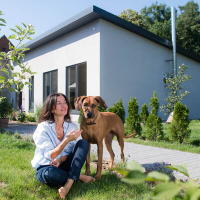 Picture of a client with her dog in front of her finished and plastered bungalow extension made of straw building modules from LORENZ